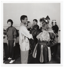 B&W photo of a small group of people dancing in pairs. Many are dressed in traditional costumes. One woman is wearing a sweatshirt with the text "Move It Or Lose It" and a logo printed on the front.