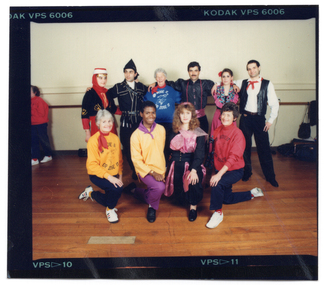 COL photo proof of a group of people posing for a Photograph.  The four people in the back row are standing, while the four people in the front row are kneeling on one knee. Many are dressed in traditional costumes, while one young man is wearing a plain tunic top and slacks with a kerchief around his neck. Three women are wearing a sweatshirt with the text "Move It Or Lose It" and a logo printed on the front.