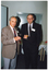COL photo of two men standing indoors, near a doorway. On the wall behind them is a butler's servery, which is closed.