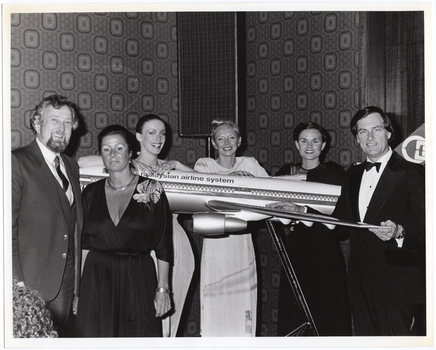 B&W photo of a small group of people gathered around a large model of a Malaysian Airlines aeroplane on a stand.