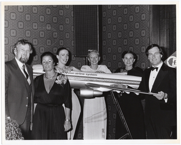 B&W photo of a small group of people gathered around a large model of a Malaysian Airlines aeroplane on a stand.