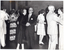 B&W photo of several couples dancing on a dance floor at an indoor venue. In the background, there is a brick wall and a curtained window.