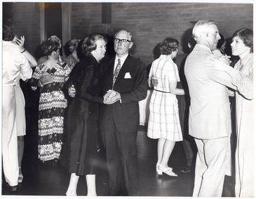B&W photo of several couples dancing on a dance floor at an indoor venue. In the background, there is a brick wall and a curtained window.