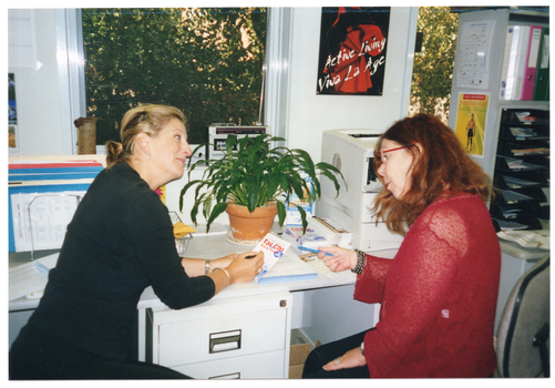 COL photo of two women, sitting at a desk, looking at a brochure which the woman on the left is holding.