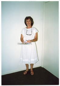 COL photo of a woman standing in the corner of a room, holding some money (notes) and leaflets.