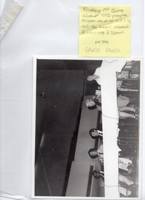 COL digital scan of a clear plastic sleeve with a handwritten yellow sticky note stuck to the top right corner, and a black and white Photograph inside it. On the note, written in pencil: "Friday 1st June about 550 people responded to R.A.A.V.'s call to hear about Arthritis & Sport 1979". On the same sticky note, handwritten in blue ink: "SPORTS PANEL".