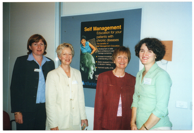 COL photo of four women standing in a row in front of an Arthritis Victoria poster on a display board. The poster is titled, "Self Management Education for your patients with chronic diseases", and sub-titled, "The benefits of self-management education".