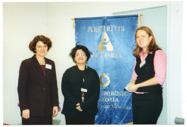COL photo of three women posing for a photo in front of a large blue and gold, freestanding, vertical banner. The banner contains the text "ARTHRITIS VICTORIA", "OSTEOPOROSIS VICTORIA", and "MUSCULOSKELETAL HEALTH", with two corresponding logos.