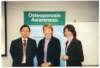 COL photo of three people posing for a photo in front of a large freestanding vertical banner. The banner contains the text heading, "Osteoporosis Awareness", followed by words such as "support", "advocacy", and "research".