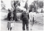 B&W photo of three people walking in or beside a park or reserve. One of them is using a walking frame.