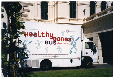 COL photo of a large white van parked outside a large white building. There are various text and logos depicted on the side of the van: "Arthritis Victoria" and "Osteoporosis Victoria" in small font, with their respective logos, at the top; "Healthy Bones Bus 1800 011 041" in large text across the centre; "Proudly donated by the Victorian Ladies' Bowling Association" and "Proudly Sponsored by PENSIONERS NETWORK" with its respective logo, both in small font at the bottom. There are also several drawings of skeletons in various sizes positioned around the text and logos.