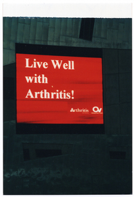 COL photo of a large electronic advertising billboard on the side of a tall building. The billboard displays white text on a red background. The text is, "Live Well with Arthritis!", with the respective text and logos for 'Arthritis Victoria' and 'Osteoporosis Victoria' below that.