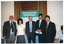 COL photo of five people standing side by side, posing for a photo. Behind them is a freestanding vertical blue and green banner, titled 'Osteoporosis Awareness'. Behind the banner is a tall window, with wooden venetian blinds and brown curtains, above a dado wall.  Behind them is a freestanding vertical blue and green banner, titled 'Osteoporosis Awareness'.