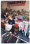 COL photo of four women inside a shop. They are sorting through clothing and other items. In the foreground, one woman is holding a small toddler's dress on a coathanger. She is looking down at the dress. There are racks of hanging clothes in front of and behind her. In the backgound, two women are holding up a crocheted blanket and a small item of clothing, respectively. They are standing behind a row of large square display bins. Another woman is standing further back in the same aisle. She is turning away from the camera. On the wall behind the three women, there is a large orange, black, and white sign just below the ceiling. The text on the sign says, "ARTHRITIS", "Something can be done!" [the word 'can' is underlined], "ARTHRITIS FOUNDATION OF VICTORIA PHONE 862 2555".