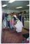 COL photo of the interior of a shop. There are several clothes racks in the centre of the room, with clothes hanging neatly from them. In the background, there is a counter, bookshelves, and some wall-mounted shelves. Various donated items have been arranged neatly on the shelving, including soft toys, baskets, some boxed items, kitchenware, and bric-a-brac.