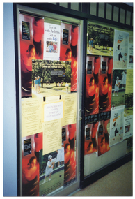 COL medium close up photo of a shop's closed glass door and large display window (partially obscured). Both the door and window are completely covered with a range of arthritis-related posters. One poster depitcs a dancer; another poster depicts a woman playing lawn bowls; another poster depicts two people walking along a path in a park; another poster depicts an illustration of a person. There are duplicate posters of each design covering the shop's door and window.