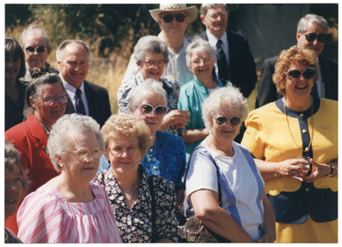 COL close up photo of a group of people outdoors. It is a sunny day and many are wearing bright coloured clothes.