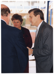 COL medium close up photo of three people talking inside a building. One person is facing the camera, one person is in profile, and the third person has his back to the camera.
