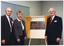 COL photo of three people standing beside a plaque, which is handing on a board resting on an easel. Across the board is a small set of gold curtains, which have been drawn open to reveal the plaque. The text on the plaque is: "ARTHRITIS FOUNDATION OF VICTORIA INC. THIS PLAQUE COMMEMORATES THE OPENING OF THE PERCY BAXTER ARTHRITIS CENTRE AND WAS UNVEILED ON THIS DAY THE 19TH OCTOBER 1994 BY HIS EXCELLENCY, THE HONOURABLE RICHARD E McGARVIE AC, GOVERNOR OF VICTORIA PRESIDENT DR LES KOADLOW ARCHITECT MR GRANT ROSE".