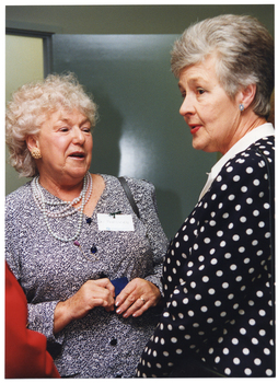 COL photo of three women (one partially obscured) standing in a room, chatting.
