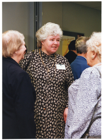 COL medium close up photo of three women chatting inside a crowded room.