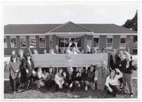 B&W photo of a group of people gathered around a large sign, which is situated in the front yard of a brick building. The text on the sign is: "ARTHRITIS FOUNDATION OF VICTORIA INC EST 1968 THE PERCY BAXTER ARTHRITIS CENTRE". Above the text is a logo.