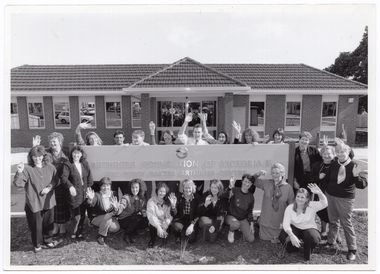 B&W photo of a group of people gathered around a large sign, which is situated in the front yard of a brick building. The text on the sign is: "ARTHRITIS FOUNDATION OF VICTORIA INC EST 1968 THE PERCY BAXTER ARTHRITIS CENTRE". Above the text is a logo.