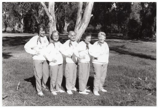 B&W photo of a five women posing for a photo in a park. They are standing close to one another in a line, at a 45 degree angle, with one hand on one hip. They are each wearing a sweatshirt printed with the "Joint Action" logo.  There are several trees in the background, with one very large tree directly behind them.