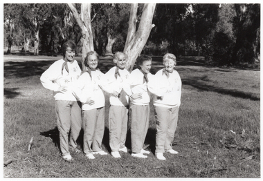 B&W photo of a five women posing for a photo in a park. They are standing close to one another in a line, at a 45 degree angle, with one hand on one hip. They are each wearing a sweatshirt printed with the "Joint Action" logo.  There are several trees in the background, with one very large tree directly behind them.
