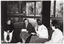 B&W photo of four women, sitting on chairs in a semi-circle. One woman is speaking while the other three women are facing her.