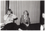 B&W photo of three women (one partially obscured), sitting on chairs in a large room. Two of the women are wearing 'Move it or Lose it' sweatshits. Behind them, there is a set of large glass sliding doors covered by closed curtains.