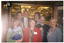 COL photo of a small group of people standing close together in two rows in the lobby of a building. There are four people in the front row, and three people in the back row. There are one or two other people (partially obscured) standing behind or beside them. In the background, inside the main hall of the venue, an ornate but modern decoratively lit ceiling is evident through a wide double doorway.