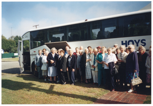 COL photo of a large group of people standing in front of a coach bus. The word "HOYS" is painted on the side of the coach. This photo has been taken from an angle, and depicts the majority of the coach, from the front. The rear end of the coach in not in frame.
