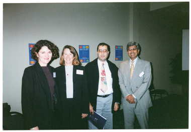 COL photo of four people standing next to one another in a row.  In the background, there are some chairs and several 'Move It Or Lose It' posters on the wall behind them.