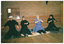 COL photo of four people lying face-up on some blankets on the wooden floor, with only their legs showing. Meanwhile, four other people are sitting across them with their knees on the blankets. Some of the people kneeling are laughing. In the background, there is a brick wall with a window, through which a storage room with some cardboard boxes is evident.