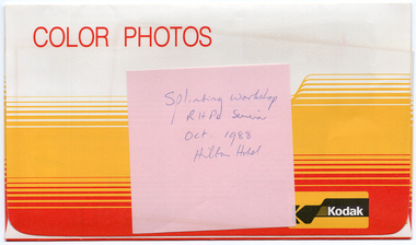 COL digital scan of a red, yellow/orange, and white Kodak photo envelope with the heading “COLOUR PHOTOS” in red text at the top of the flap, and the Kodak logo in the bottom right hand corner of the flap. There is a handwritten pink sticky note stuck to the top of the flap.