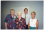 COL medium close up photo of four people standing close together in a room. There is a large whiteboard affixed to the wall behind them.