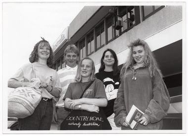 B&W photo of five teenagers standing in two rows outside an airport terminal. A sign on the terminal building (partially obscured) says "...Australia". The photo has been taken from a low angle.