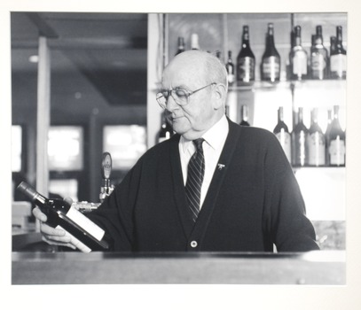 Portrait of a man behind a bar looking at a bottle of wine. 