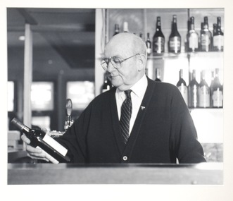 Portrait of a man behind a bar looking at a bottle of wine. 