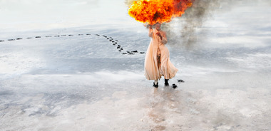 Photograph of figure with burning material in snow scape. 