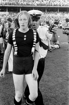 A black and white photo of a police office and fan on a football field. 