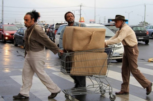 Three men pushing a shopping trolley over a pedestrian crossing.