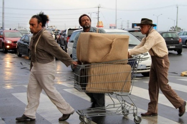 Three men pushing a shopping trolley over a pedestrian crossing.