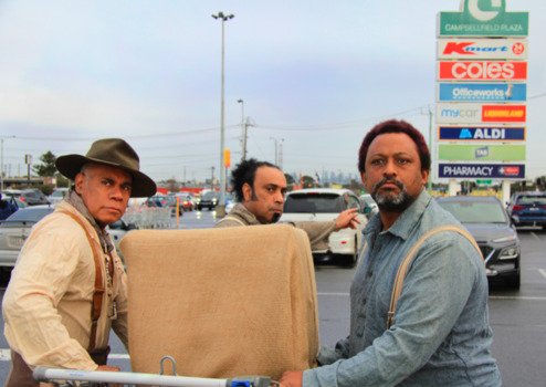 Three men pushing a shopping trolley over a pedestrian crossing.