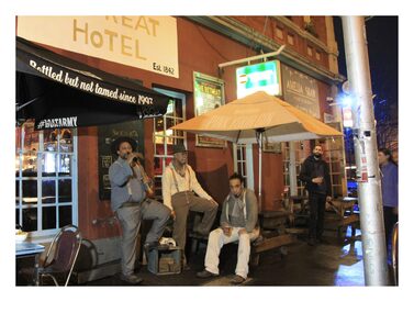 Three men having a drink out the front of a pub. One is holding a axe.
