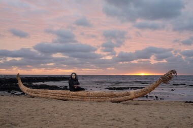  First Nations artist Maree Clarke on the beach sitting on a traditional river reed canoe.