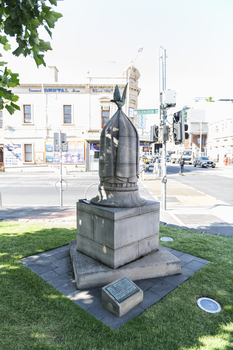 A large sculpture of a stone cut birdcage - there is a sheet covering the birdcage with a with a bronze bird lifting it off. 