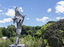 A statue of a naked man waving a piece of cloth throwing his hands up in the air. The whole statue including the cloth is cast in bronze.