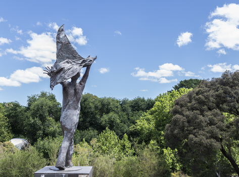 A statue of a naked man waving a piece of cloth throwing his hands up in the air. The whole statue including the cloth is cast in bronze.